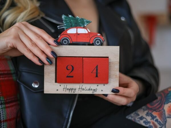 A woman holds a festive countdown sign for December 24th, with a car carrying a tree. Perfect for holiday cards.