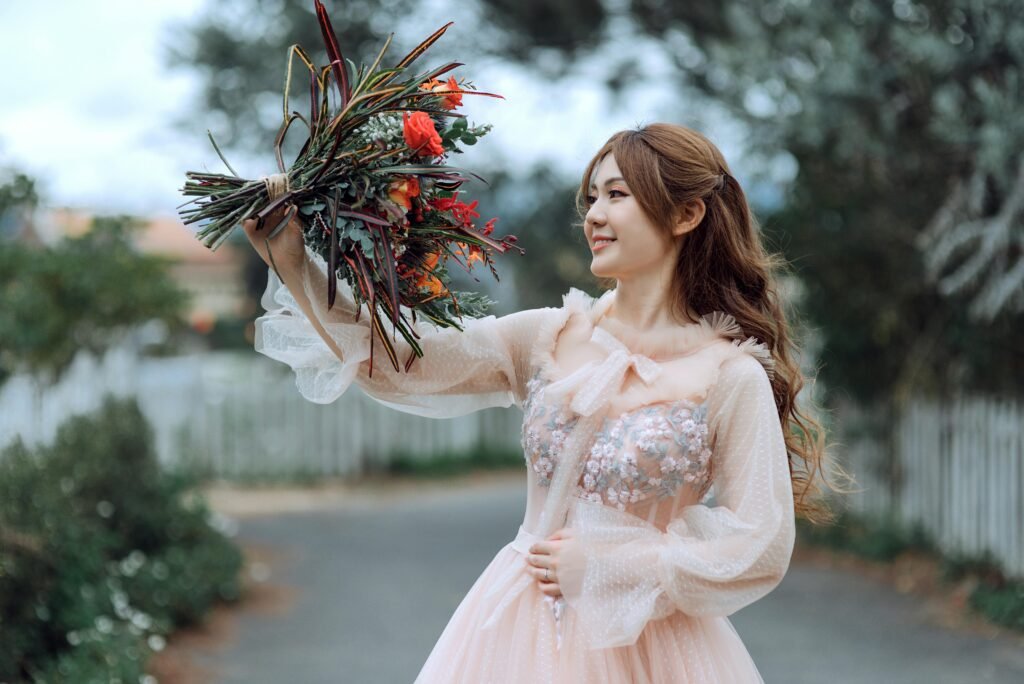A beautiful woman in a delicate dress holds a vibrant floral bouquet outdoors, expressing joy.
