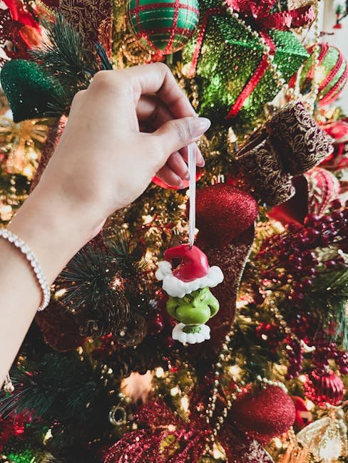 Hand placing Santa and Grinch ornament on decorated Christmas tree.